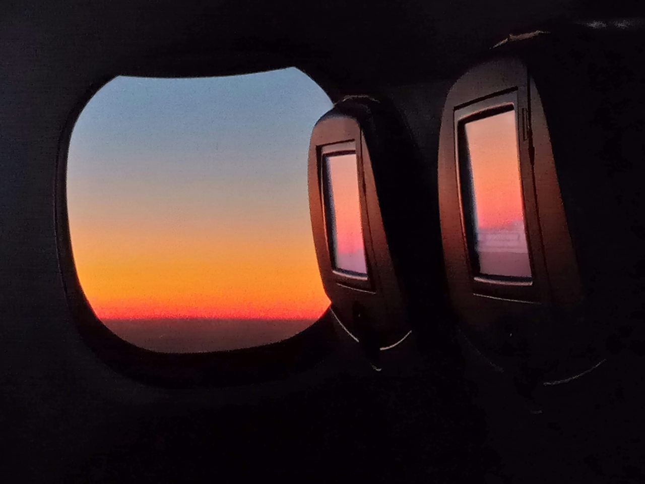 A dark aircraft cabin, the window glowing with sunrise