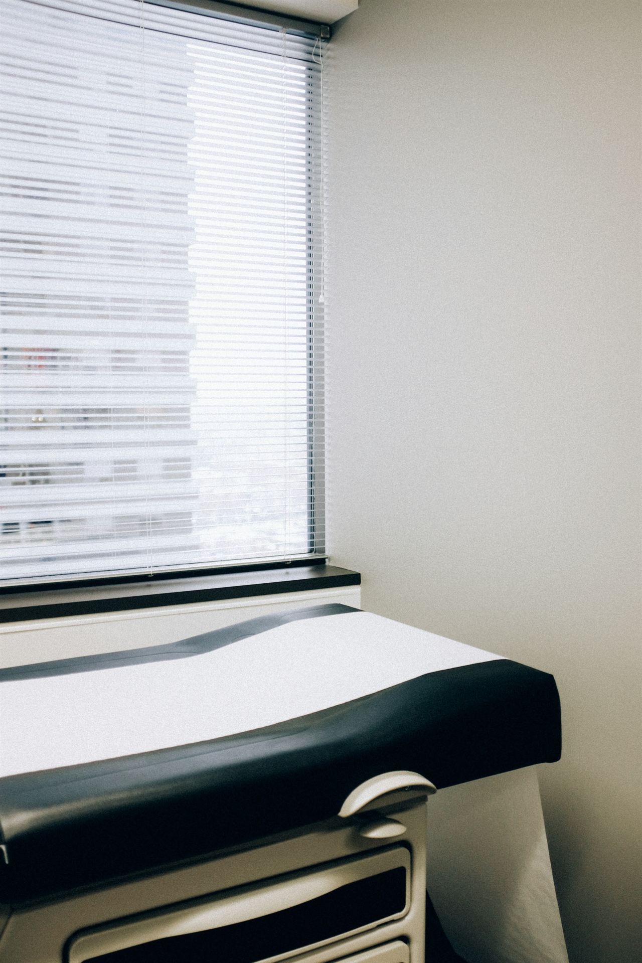 A quiet examination room with an empty table beside a window with blinds