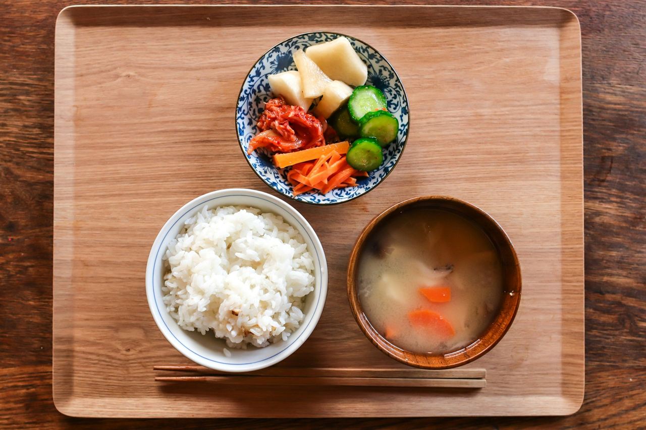A wooden tray with a bowl of rice, a bowl of miso soup and a small dish of pickles