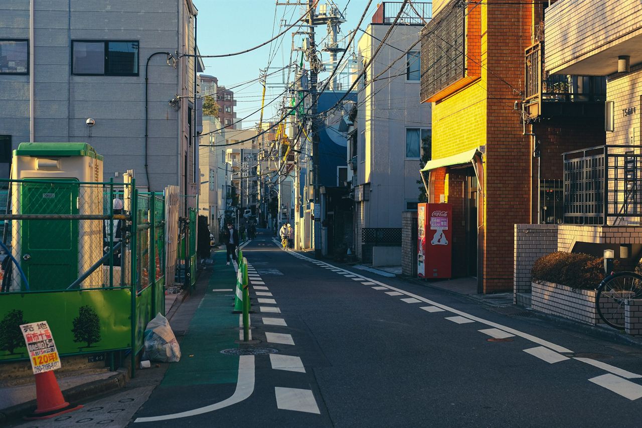 A quiet Tokyo side street by day, with overhead wires and a red vending machine