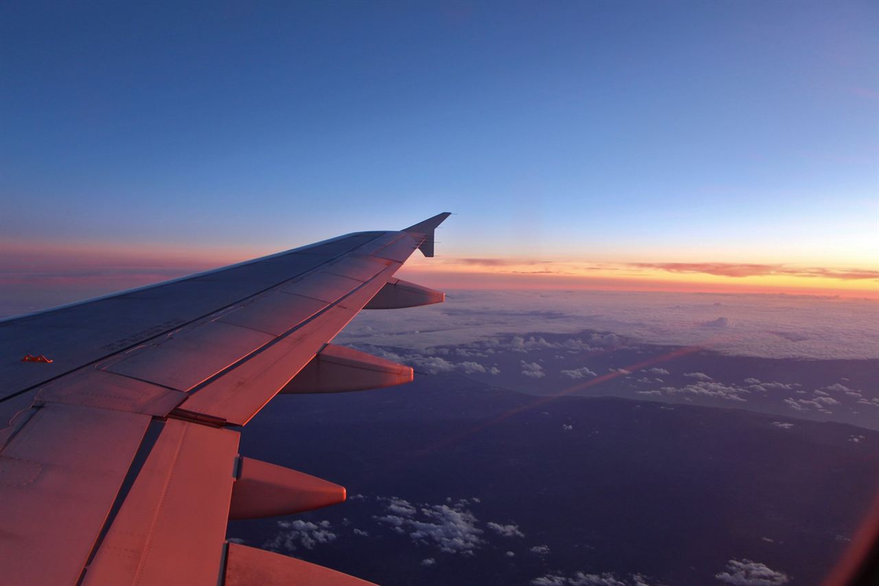 An aircraft wing at dusk, the horizon glowing orange below a deep blue sky